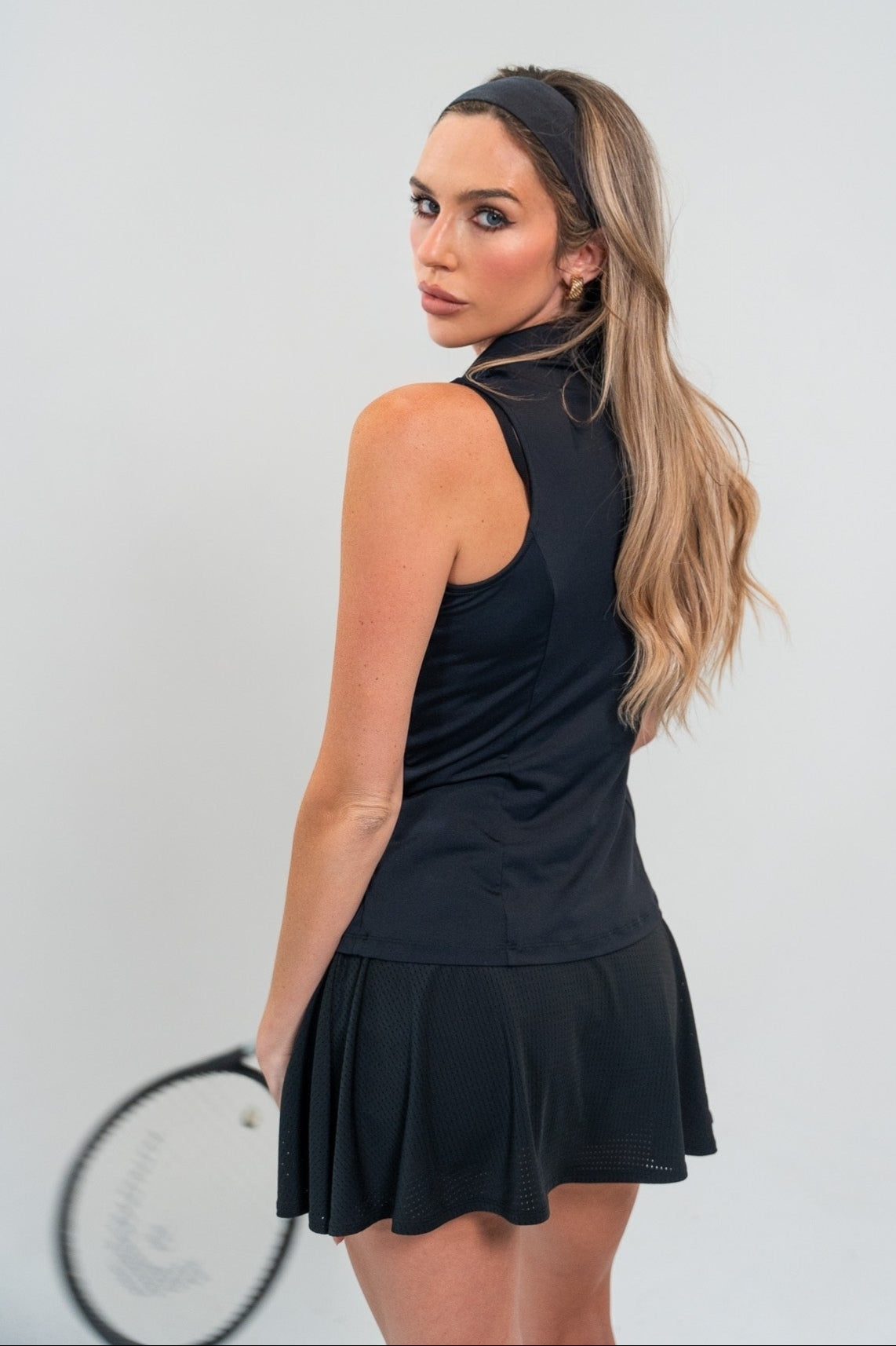 Woman in a black tennis outfit holding a racket against a white background